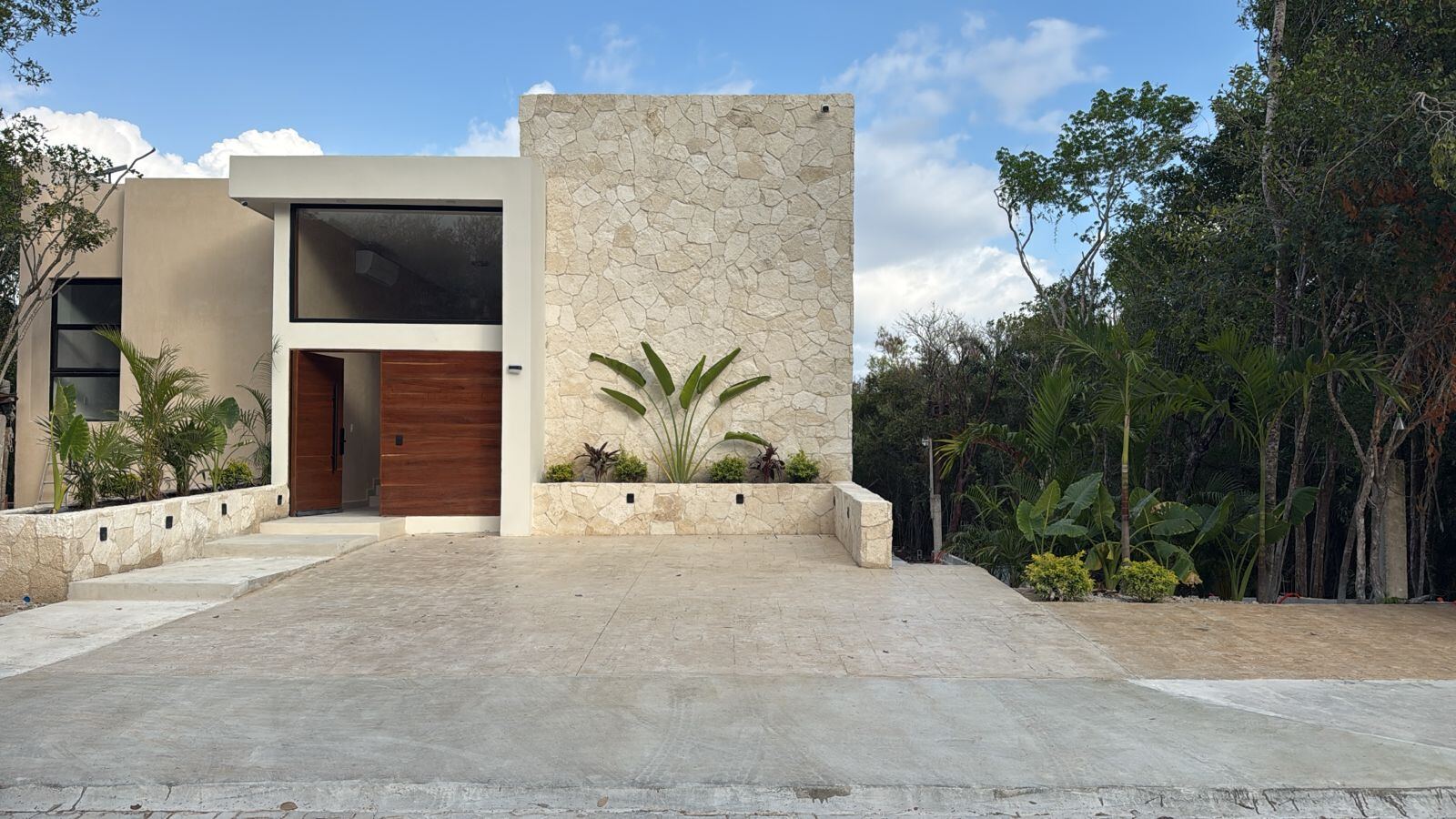 Stone-clad entry with oversized Tzalam wood door beneath a window of equal scale