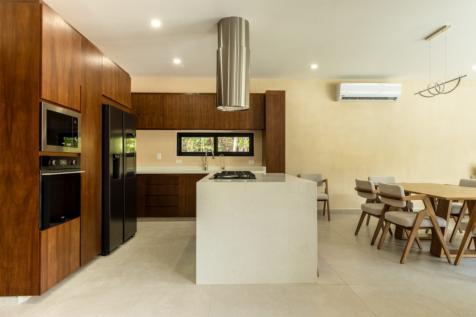 Open kitchen with wood cabinetry, stone island and gas hob, opening onto a dining table